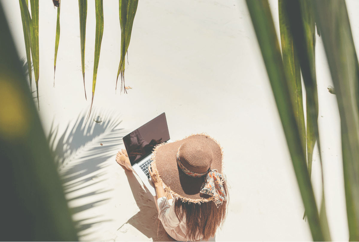 woman wearing hat on the beach with her laptop